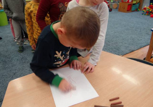 Dziecko kalkuje obrazek pocierając kredką karton nałożony na trójwymiarowy kontur.